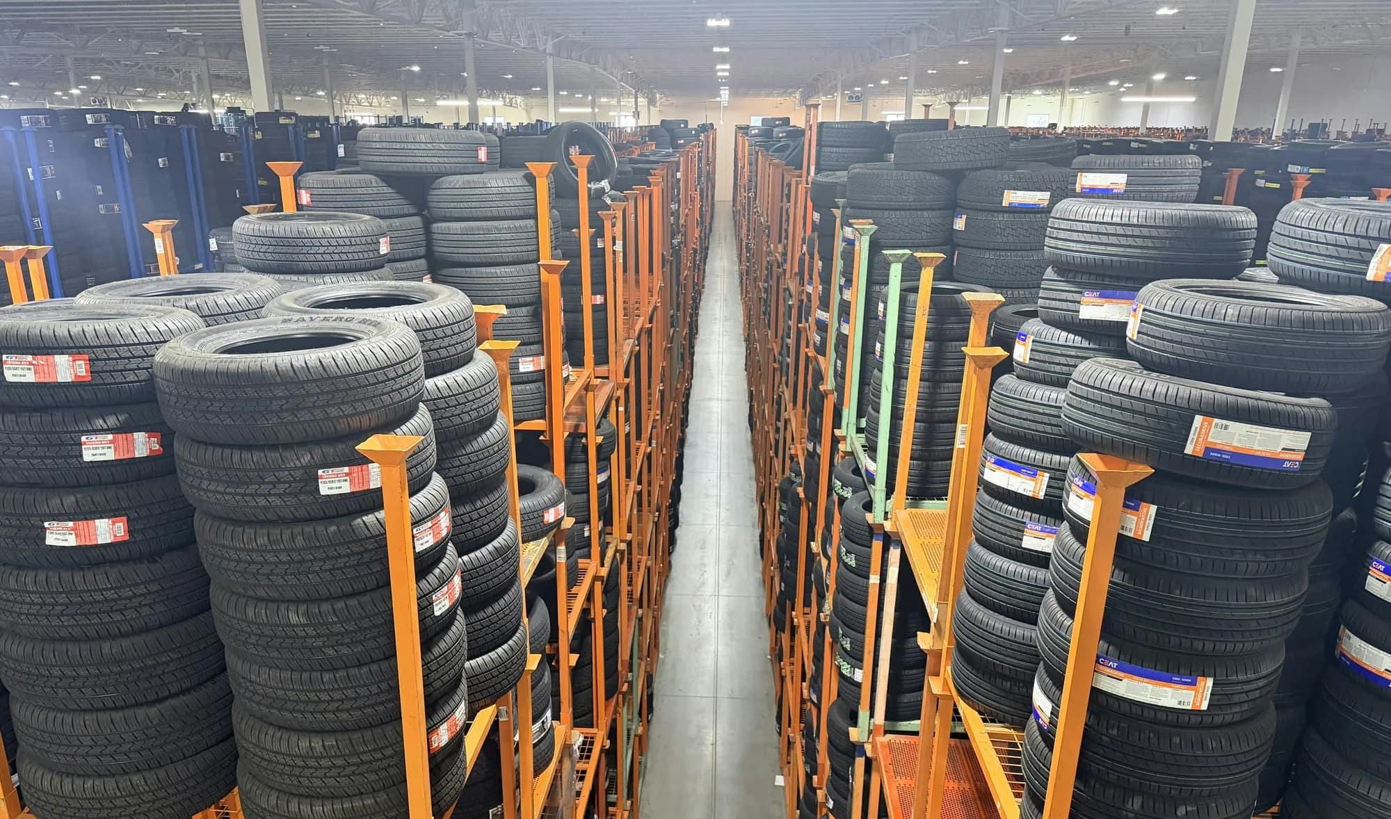 A long warehouse aisle lined with orange racks stacked high with passenger tires