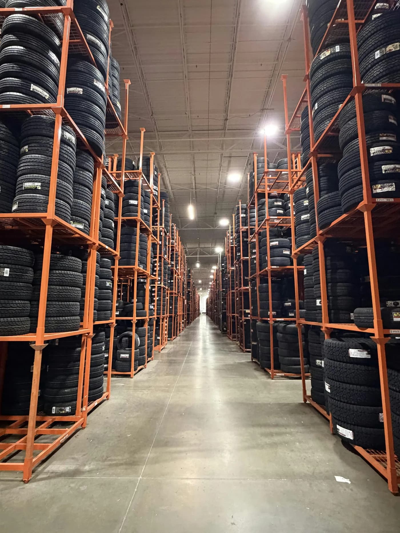 A long warehouse aisle between tall orange racks stacked with tires